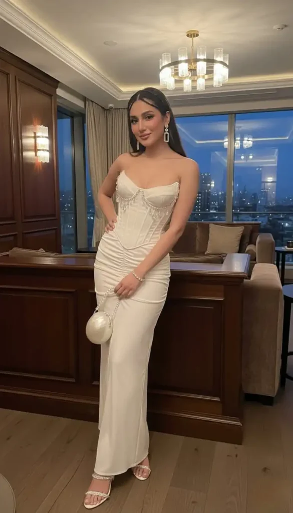 Woman in fitted white dress with pearl-drip corset bodice and round pearl bag.